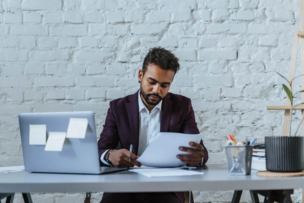 A person reviewing notes and a laptop screen while reading through information carefully